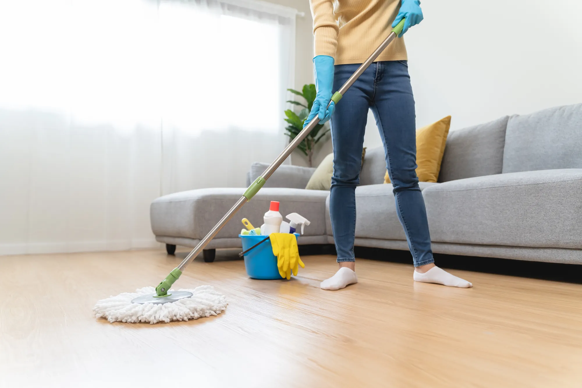 Colaboradora passando o mop no piso de uma sala clara e arejada